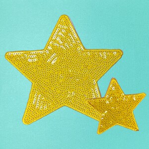 May include: Two gold sequined stars on a turquoise background. The larger star is on top of the smaller star.