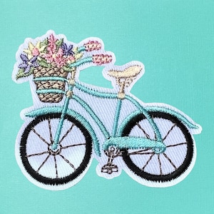 May include: A turquoise blue bicycle with a basket full of colorful flowers. The bicycle has a white seat and black tires.