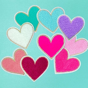 May include: Nine felt heart-shaped patches with gold trim. The hearts are in various colors, including pink, red, white, purple, blue, and turquoise.
