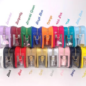 May include: A row of 15 clear plastic zippered pouches with different colored exteriors. The pouches are lined up in a row from left to right. The colors are purple, lavender, burgundy, emerald green, royal blue, orange, hot pink, teal, baby blue, white, black, red, tan, gold, silver, pink, navy, and yellow.
