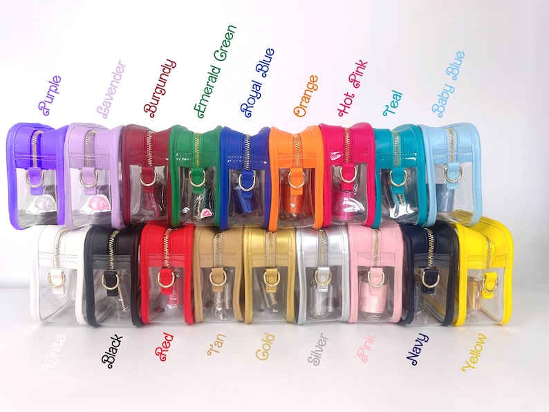 May include: A row of 15 clear plastic zippered pouches with different colored exteriors. The pouches are lined up in a row from left to right. The colors are purple, lavender, burgundy, emerald green, royal blue, orange, hot pink, teal, baby blue, white, black, red, tan, gold, silver, pink, navy, and yellow.