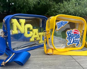 May include: Two clear plastic crossbody bags with yellow and blue straps. The bag on the left has a yellow felt "NCAT" patch. The bag on the right has a yellow felt "Game Day" patch with a football graphic and a blue felt "GAMEDAY" patch.