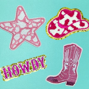 May include: Four pink and white embroidered iron-on patches with gold glitter trim. The patches include a cowboy hat, a boot, a star, and the word "Howdy".