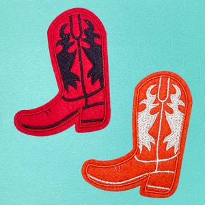 May include: Two felt cowboy boot patches. One is red with black embroidery and the other is orange with white embroidery.