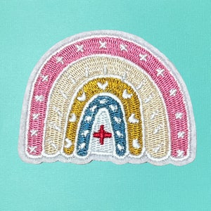 May include: A rainbow-colored embroidered patch with a white cross in the center. The rainbow is made up of pink, beige, yellow, blue, and white.