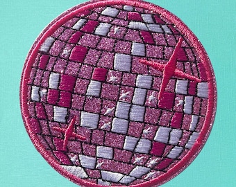 May include: A pink and white glitter disco ball patch with a pink outline. The patch is round and has a textured surface.
