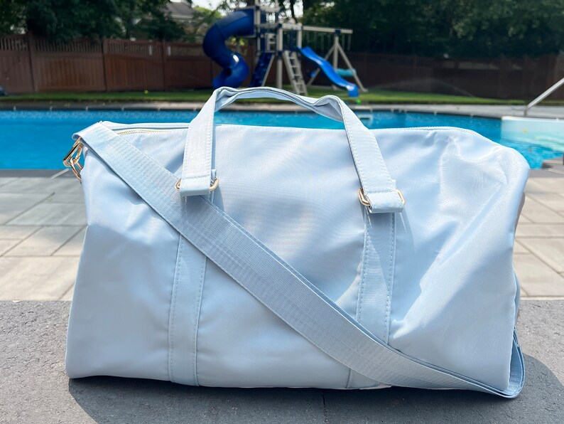 May include: A light blue duffel bag with a gold zipper and gold hardware. The bag has a long strap that can be worn over the shoulder.