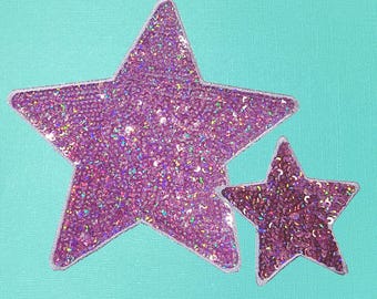 May include: Two sparkly pink star-shaped patches. The larger star is slightly larger than the smaller star.