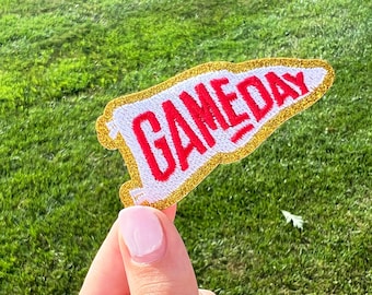 May include: A white felt pennant with gold glitter trim and the word "GAMEDAY" embroidered in red.