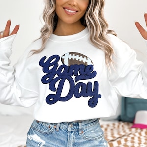 May include: White sweatshirt with a navy blue "Game Day" graphic and a brown football graphic.