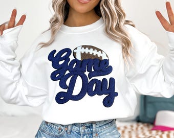 May include: White sweatshirt with a navy blue "Game Day" graphic and a brown football graphic.
