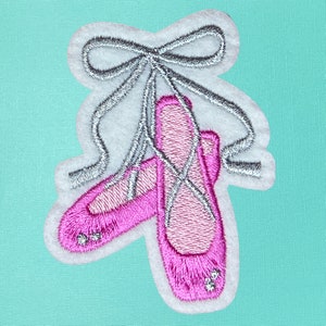 May include: A pair of pink ballet shoes with a silver ribbon tied around them. The shoes are embroidered with a sparkly design.