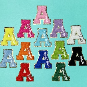 May include: A set of 12 felt letter patches in various colors, including black, white, pink, purple, green, orange, red, yellow, sky blue, lake blue, and royal blue. Each patch features a gold outline and the letter "A" in a varsity style font.