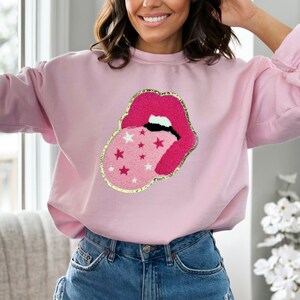 May include: Pink sweatshirt with a large embroidered patch of a pink and red tongue sticking out of a mouth with white stars on the tongue.