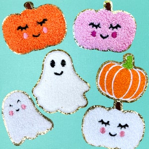 May include: A collection of six embroidered patches featuring three pumpkins with smiling faces in orange, pink, and white, one orange pumpkin with green stem, and two white ghosts with smiling faces, all outlined with a gold metallic thread border.