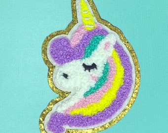 May include: A purple, pink, yellow, and green unicorn applique with a gold glitter outline. The unicorn has a closed eye and a yellow horn.