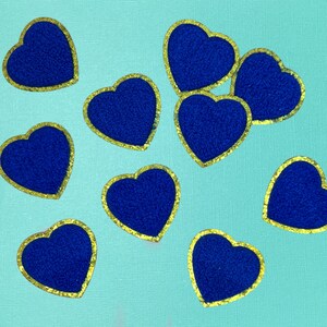 May include: Ten blue felt hearts with gold glitter trim. The hearts are scattered on a light blue background.