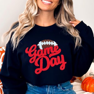 May include: Black sweatshirt with a red "Game Day" graphic and a brown football graphic.