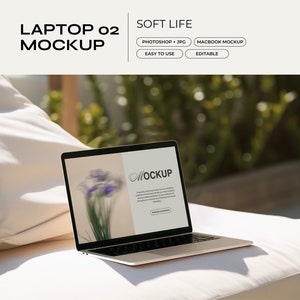 May include: A silver laptop computer with a white background on the screen. The screen shows the word "MOCKUP" in a cursive font. The laptop is sitting on a white cushion.