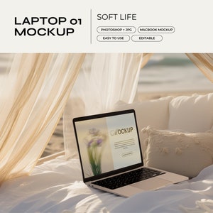 May include: A laptop computer with a white background on the screen is open on a white bed with a white pillow and a tan throw pillow. The bed is in a canopy bed with white sheer curtains. The laptop is on a beach with the ocean in the background.