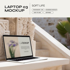 May include: A silver laptop computer with a white background on the screen. The screen shows a mockup of a website with the word "MOCKUP" in a circle. The laptop is sitting on a white surface in front of a stone wall.