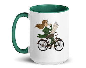 May include: White ceramic mug with a green rim. The mug features a cartoon illustration of a person riding a bicycle while reading a newspaper and holding a cup of coffee.