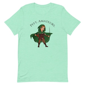 May include: A green t-shirt with a cartoon image of a female archer wearing a green hooded cloak and holding a bow and arrow. The text "PFFT. AMATEURS." is printed on the shirt.