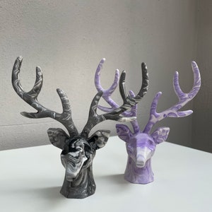 May include: Two decorative deer head sculptures, one with a black and white marbled finish and the other with a purple and white marbled finish.