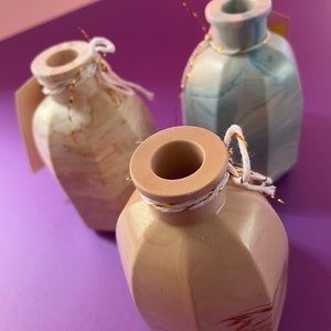 Könnte beinhalten: Drei kleine dekorative Vasen mit Marmormuster. Die Vasen sind in den Farben Rosa, Blau und Weiß gehalten. Jede Vase hat eine goldene Schnur um den Hals gebunden.