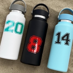 May include: Three insulated water bottles in white, black, and light blue. Each bottle has a number in a collegiate font: 20 in teal, 8 in red, and 14 in black. The bottles have a handle and a screw-on lid.