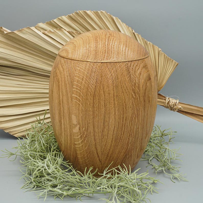 May include: A light brown wooden urn with a smooth, rounded shape. The urn is made of natural wood and has a subtle grain pattern.