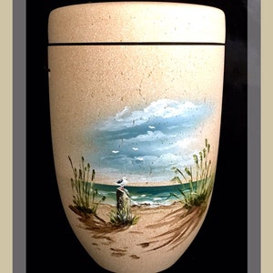 May include: A beige, urn-shaped container with a painted beach scene. The artwork depicts a blue sky with clouds, a sandy beach, ocean waves, and a seagull perched on a wooden post. The container has a black band around the top.