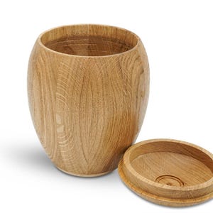 May include: A wooden storage container with a lid. The container is made of light brown wood and has a rounded shape. The lid is also made of wood and has a smooth surface.