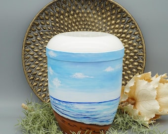 May include: White ceramic urn with a hand-painted design of a blue sky, white clouds, and a blue ocean with brown sand and footprints.