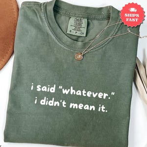 Może przedstawiać: Koszulka z krótkim rękawem w kolorze mchu z białym nadrukiem i said "whatever." i didn't mean it. T-shirt posiada okrągły dekolt, metkę marki Comfort Colors wewnątrz kołnierza oraz cienki naszyjnik na łańcuszku w odcieniu złota.