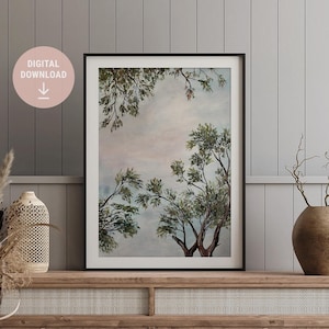 Op de afbeelding: Een digitale download van een aquarel schilderij van bomen tegen een bewolkte lucht. Het schilderij is ingelijst in een zwart frame en hangt aan een muur.