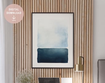 May include: A framed abstract watercolor painting with a blue and white color scheme hangs on a wall with wood paneling. A gold desk lamp sits on a white desk with a laptop, a white frame, and a small plant.