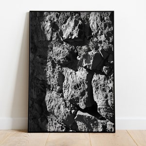 May include: Black and white framed print featuring a close-up of a textured rock face. The image captures the rough, uneven surface of the stone, with shadows adding depth and dimension. The artwork is mounted in a black frame.