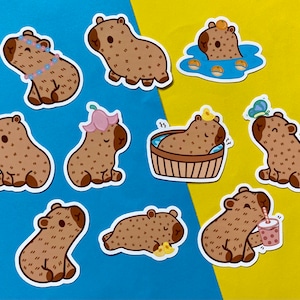 Peut inclure: Un ensemble de dix autocollants colorés représentant des capybaras de dessin animé dans différentes poses. Les capybaras portent des accessoires comme des couronnes de fleurs et des lunettes de soleil, et certains tiennent des boissons ou se détendent dans une baignoire. Les autocollants sont parfaits pour ajouter une touche de fantaisie aux ordinateurs portables, aux bouteilles d'eau ou aux journaux.
