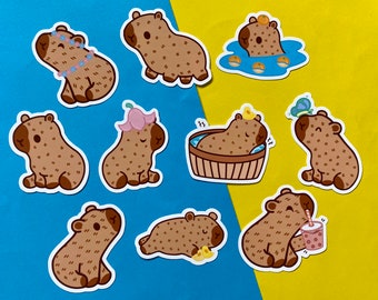 May include: A set of ten colorful stickers featuring cartoon capybaras in various poses. The capybaras are wearing accessories like flower crowns and sunglasses, and some are holding drinks or relaxing in a bathtub. The stickers are perfect for adding a touch of whimsy to laptops, water bottles, or journals.