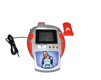 May include: A silver and red handheld electronic game console featuring a digital screen displaying the text DATE 01. 0:98. The device includes a graphic of Stone Cold Steve Austin, several red control buttons, a black wired connector, and a detached red battery cover.