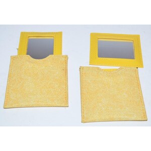 May include: Two square yellow fabric pouches, each featuring a rectangular mirror framed in matching yellow material. The pouches have a textured, woven appearance with a semi-circular cutout at the top edge for easy access to the mirror insert.