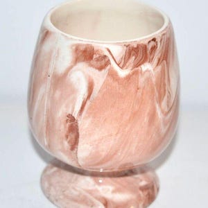 May include: A brown and white marbled ceramic planter with a pedestal base. The planter has a smooth, glazed finish.