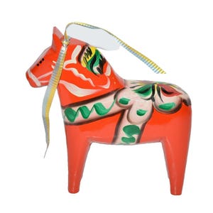 May include: A bright orange wooden horse figurine featuring hand-painted floral details in green, white, and black. The horse has a glossy finish and includes a decorative metallic gold and white ribbon attached to its mane for hanging purposes.