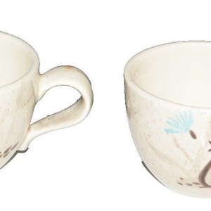 Puede incluir: Dos tazas de café de cerámica blanquecina con acabado moteado. Cada taza presenta un diseño de pájaro en azul y marrón. Las tazas tienen forma redondeada y un asa curva.