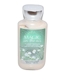 Puede incluir: Una botella de loción corporal hidratante "Magic in the Air" de Bath & Body Works. La etiqueta presenta un fondo verde azulado con detalles florales blancos y el nombre del producto. La botella contiene 236 ml de loción.