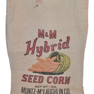 May include: A vintage burlap sack for seed corn. The sack is printed with the text "M&M Hybrid Seed Corn", "Net Wt. 1 Bu.", "Muntz-M'Laughlin Co.", and "Holgate, Ohio". The sack features a graphic of corn ears in a wooden bucket.