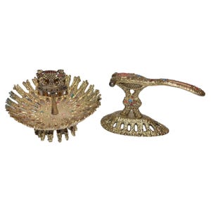 May include: Two ornate, gold-coloured metal objects. One is a round, openwork dish with a central, decorative element and colourful jewels. The other is a handle-shaped piece with a decorative base and colourful jewels. Both items have a textured surface.