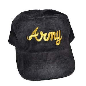 Può includere: Cappellino da baseball in velluto a coste nero con la scritta "Army" ricamata in oro sul davanti. Il cappellino ha una visiera curva e una corona strutturata. Il tessuto ha una trama a coste.