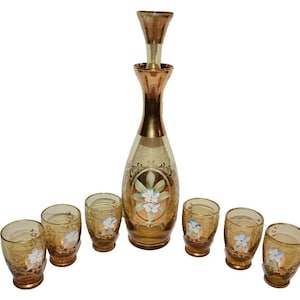 May include: A set of amber glass decanter and shot glasses with gold accents and floral designs. The decanter has a removable stopper.